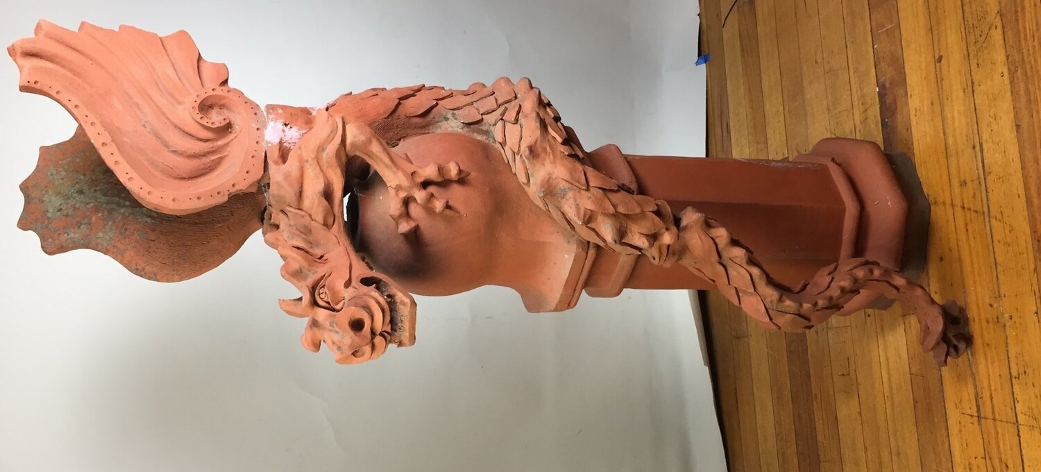 A salvaged terracotta griffin finial with deep patina, evoking the traditional hand-finishing done in the workshop