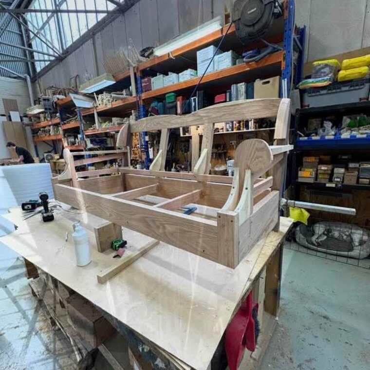 A bare timber sofa frame on the workshop bench, stripped back to the carcass